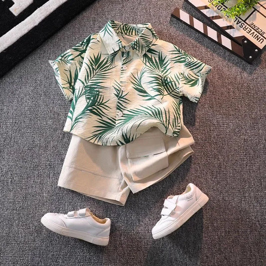 Children's outfit with leaf-patterned shirt and shorts, paired with white sneakers on a textured surface.
