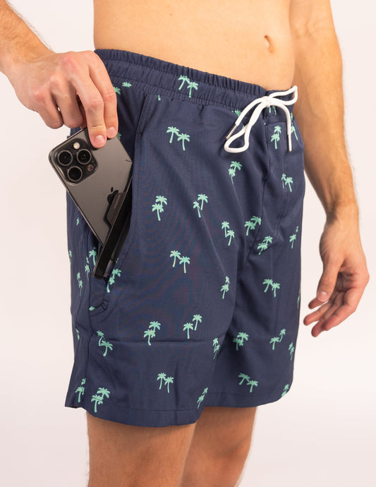 Person wearing navy swim shorts with palm tree pattern, holding a phone.