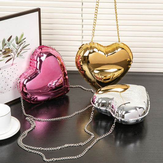 Heart-shaped handbags in pink, gold, and silver on a dark surface with a blurred background.