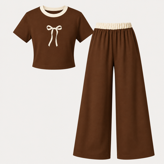 A two-piece children's outfit set featuring a brown short-sleeve crop top with a cream-colored collar and bow graphic, paired with matching wide-leg brown pants that have a cream elastic waistband, displayed on a light off-white background.