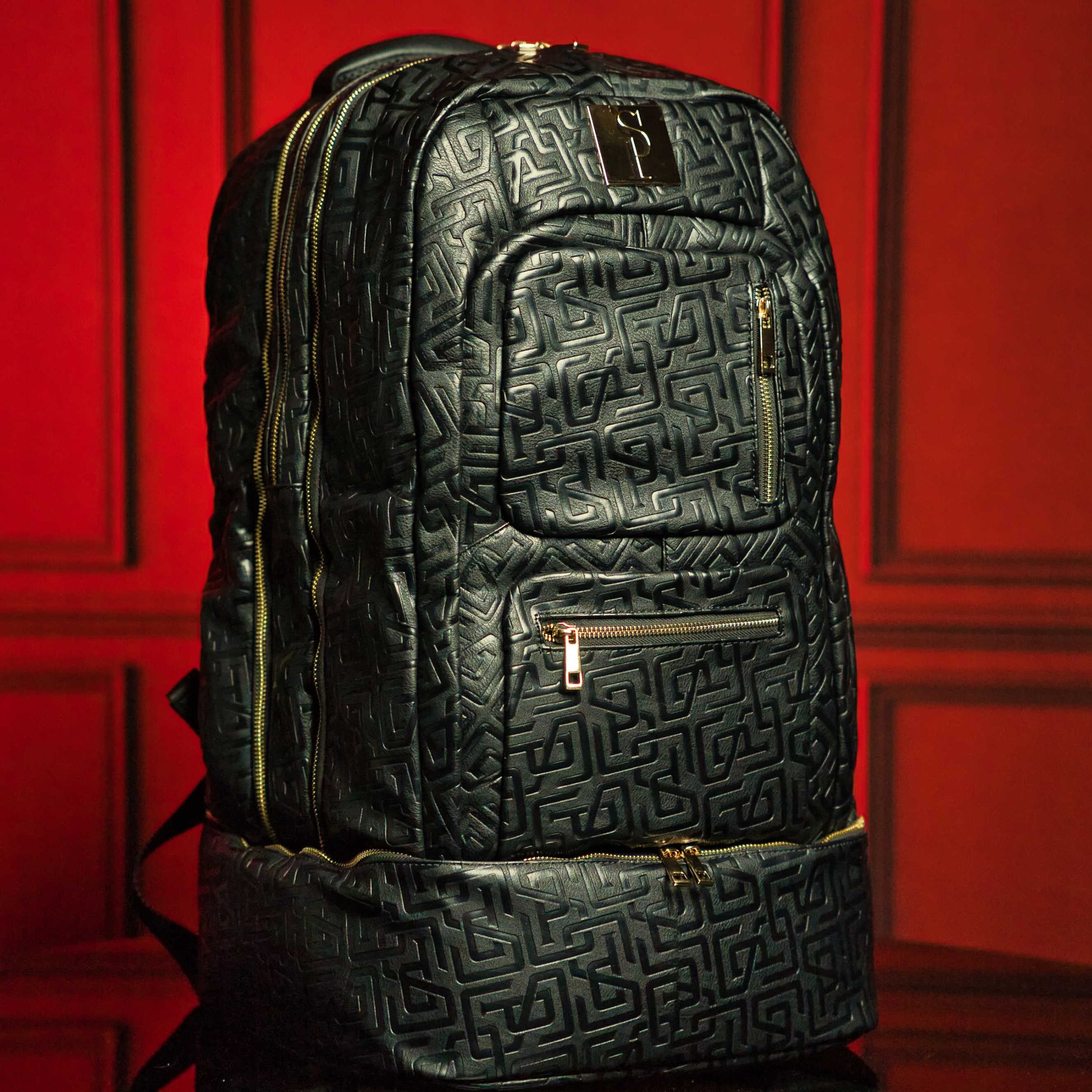 Black textured backpack with gold zippers on a red background