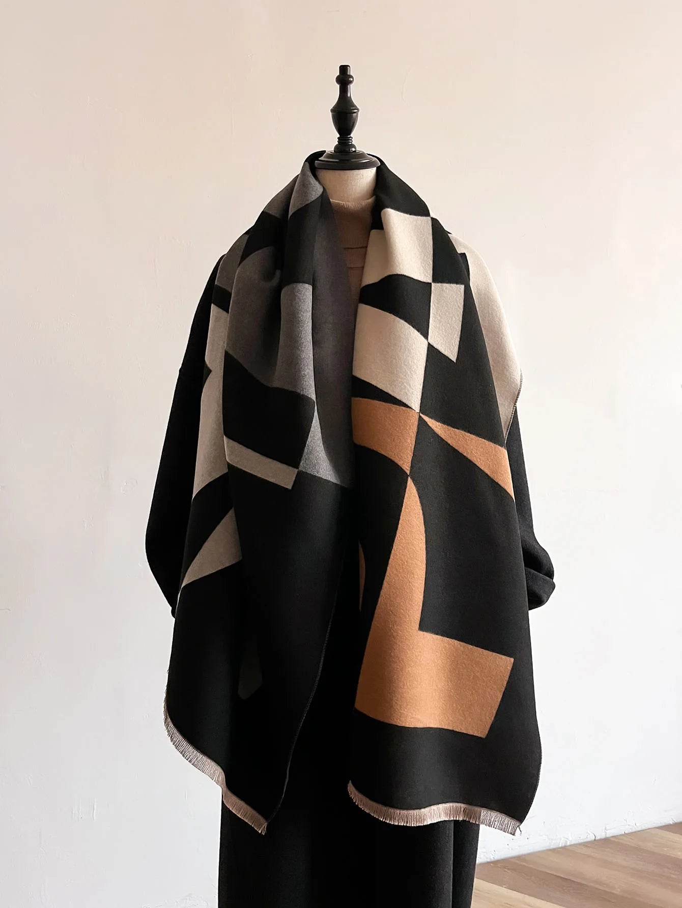 Mannequin wearing a black, brown, and beige patterned scarf against a plain background