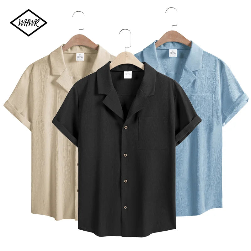Men’s short sleeve cotton button-up shirts in beige, black, and light blue on wooden hangers.