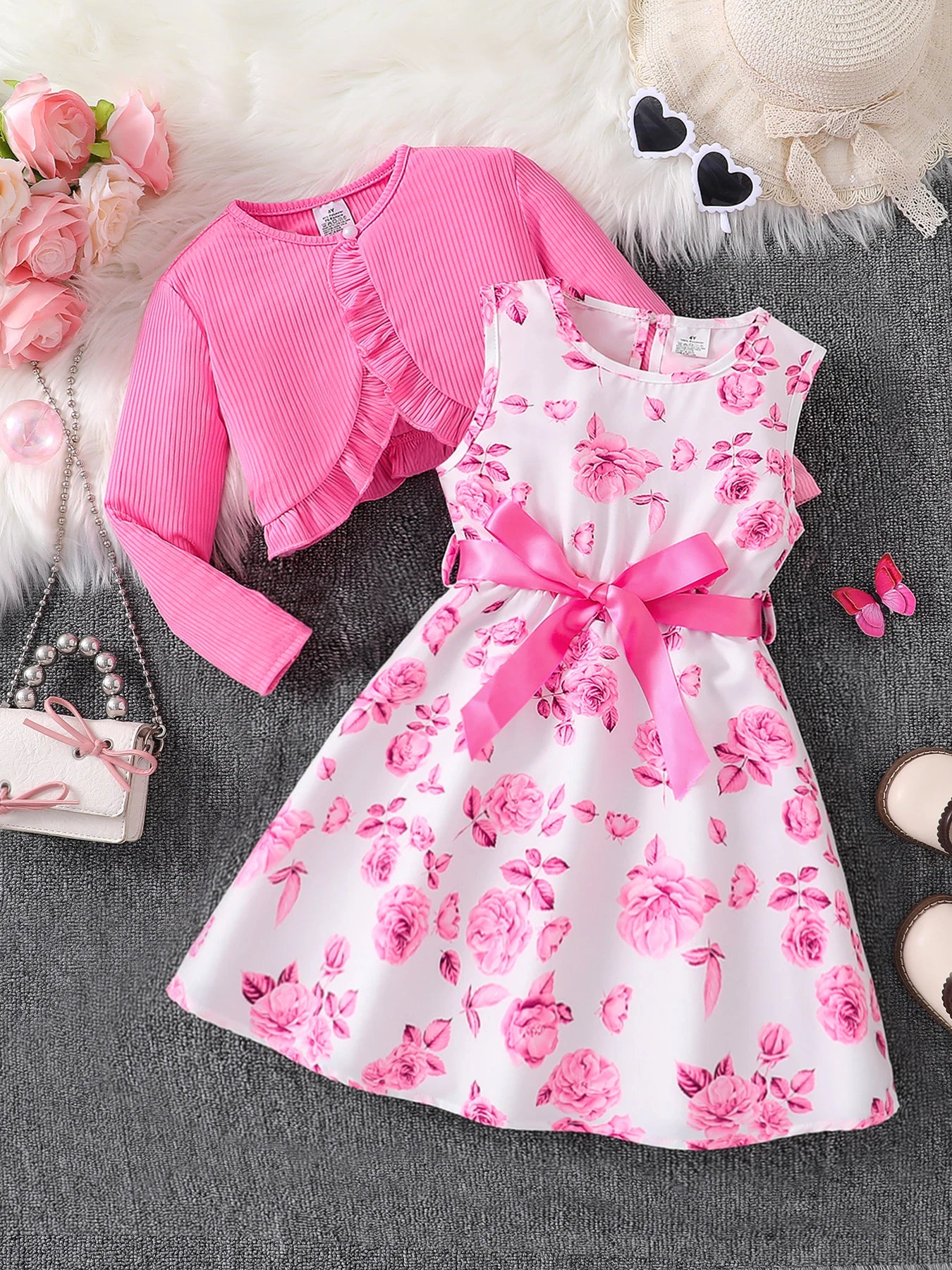 Pink floral dress with matching cardigan on a textured surface with decorative items.