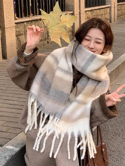 Woman wearing a large plaid scarf outdoors, holding a leaf.