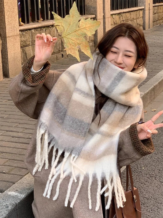 Woman wearing a large plaid scarf outdoors, holding a leaf.