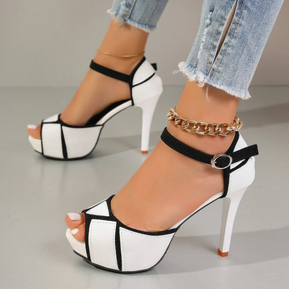 White and black platform high-heeled sandals worn with denim jeans on a neutral background