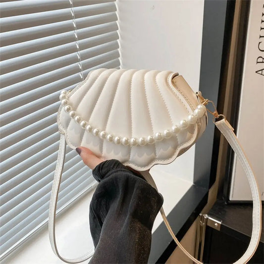 White handbag with pearl details held by a person in front of a window.