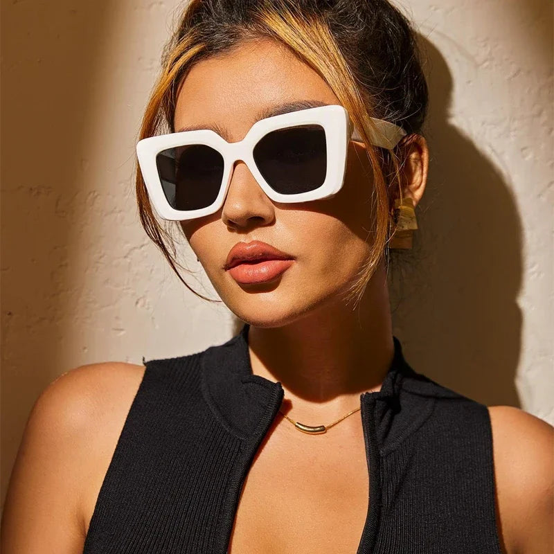 Woman wearing white sunglasses against a textured beige wall