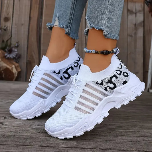 White sneakers with black and gray accents worn by a person on a wooden floor.