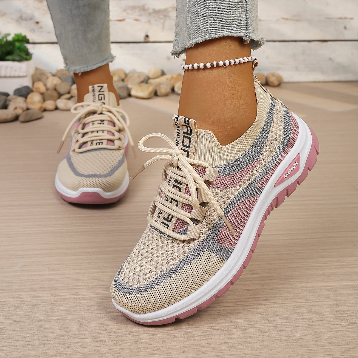 Beige and pink sneakers with white laces on a wooden floor.