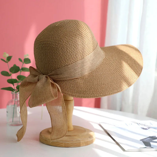 Brown straw hat with a wide brim and ribbon on a mannequin head against a pink and white background.