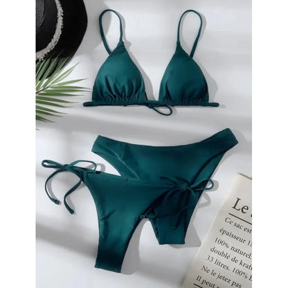 Teal bikini set on a white surface with a hat and leaf in the background