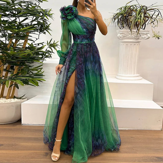 Woman wearing a green and purple dress with a slit, standing indoors with plants in the background.