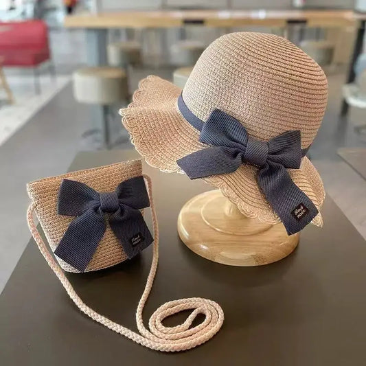 Kids straw hat with navy bow and matching crossbody bag on table