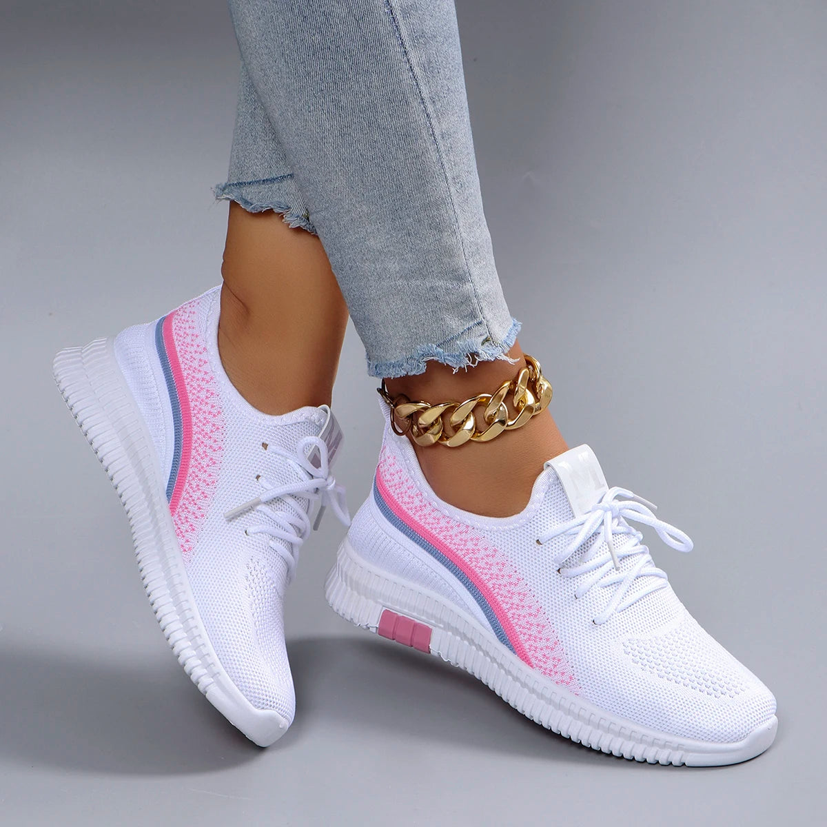 White sneakers with pink accents worn by a person on a gray background
