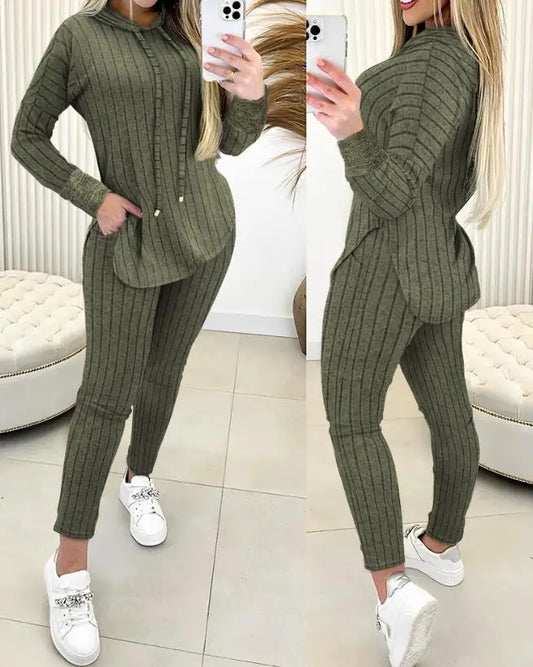 Person wearing a green ribbed sweater and pants set, standing in a room with white furniture.