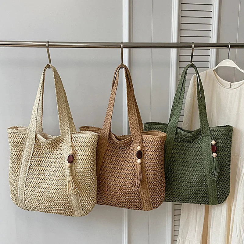 Light brown woven straw tote bag with double handles and tassel charm on display box