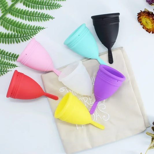 Set of colorful silicone menstrual cups on a white background with greenery.