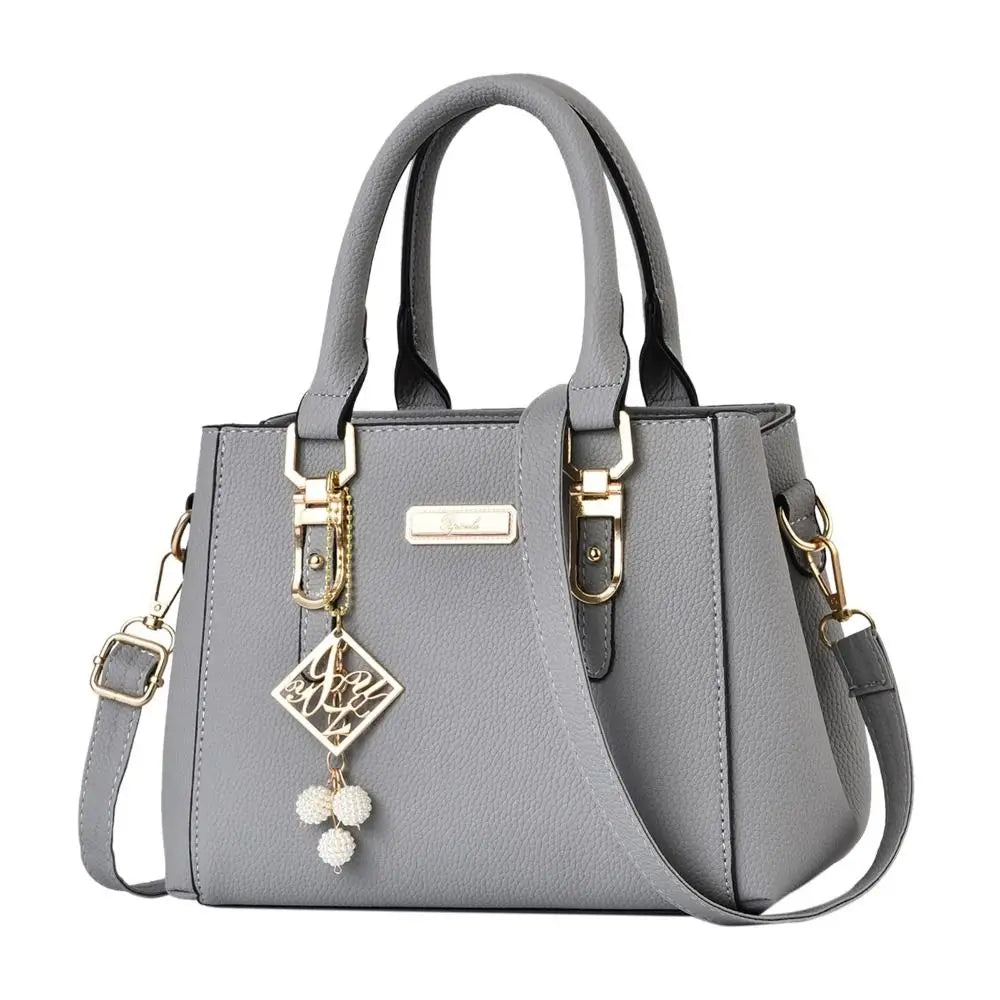 Gray handbag with gold accents and a decorative charm on a white background