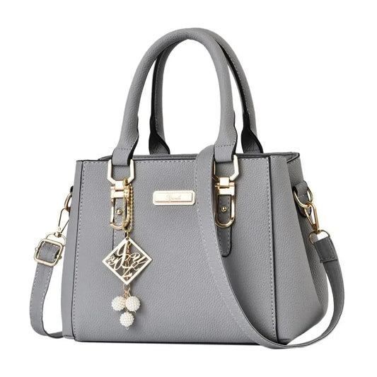 Gray handbag with gold accents and a decorative charm on a white background