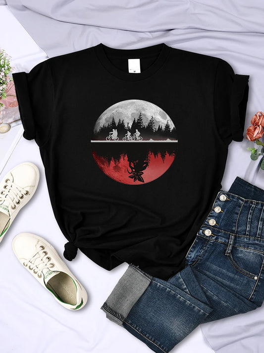 Black t-shirt with a graphic design of a campfire, trees, and a moon on a white surface with jeans and shoes.