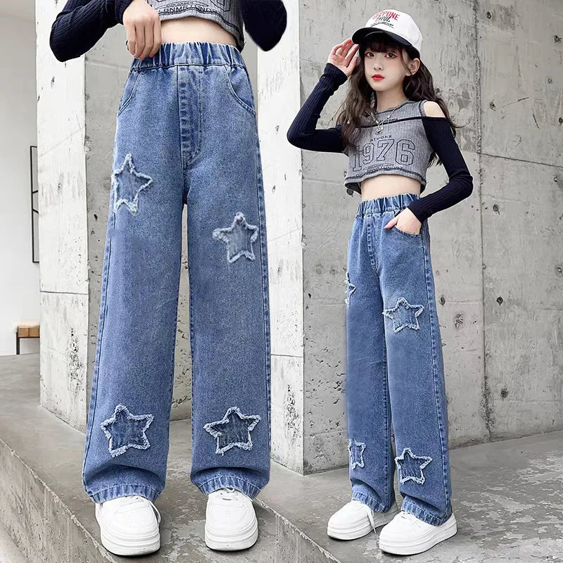 Person wearing blue jeans with star patches in front of a concrete wall.