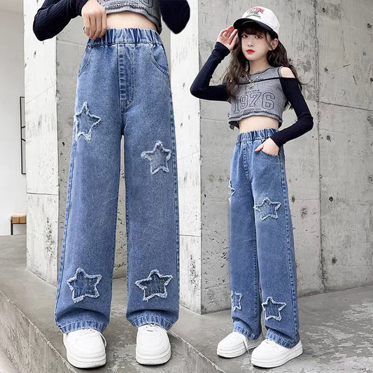 Person wearing blue jeans with star patches in front of a concrete wall.