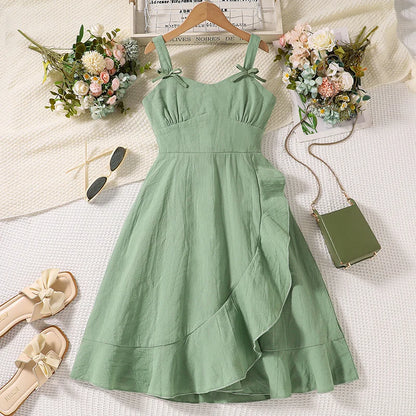 Green dress on a hanger with flowers, sandals, and a handbag on a light background