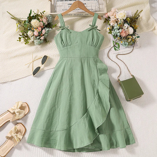 Green dress on a hanger with flowers, sandals, and a handbag on a light background