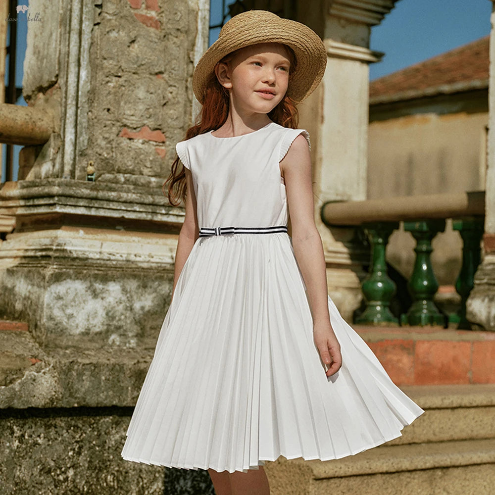Young girl in a white dress with a straw hat standing in front of an old stone building.