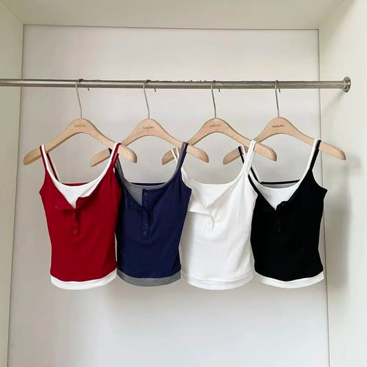 Four tank tops in red, blue, white, and black hanging on a rack against a white wall.