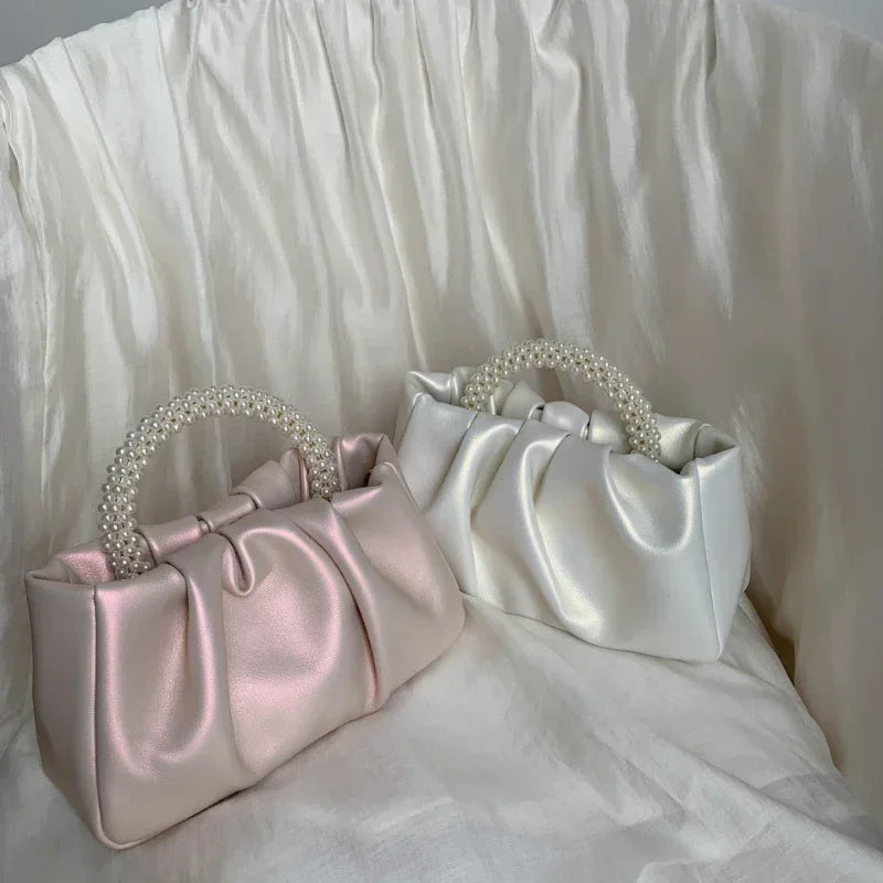 Two satin handbags, one pink and one white, with pearl handles on a white fabric background.