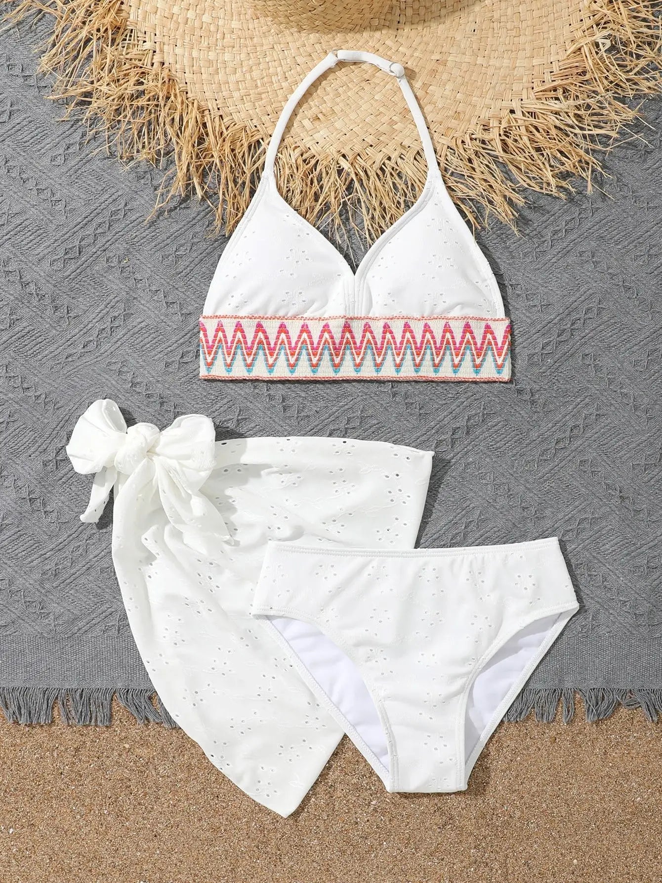 White bikini set with red and pink embroidery on a textured surface