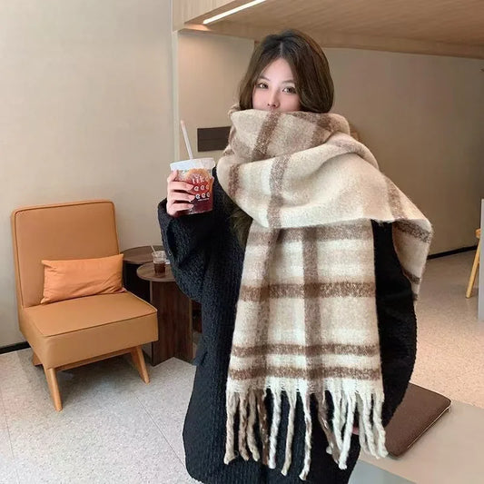 Person wearing a large plaid scarf holding a drink in a casual indoor setting.