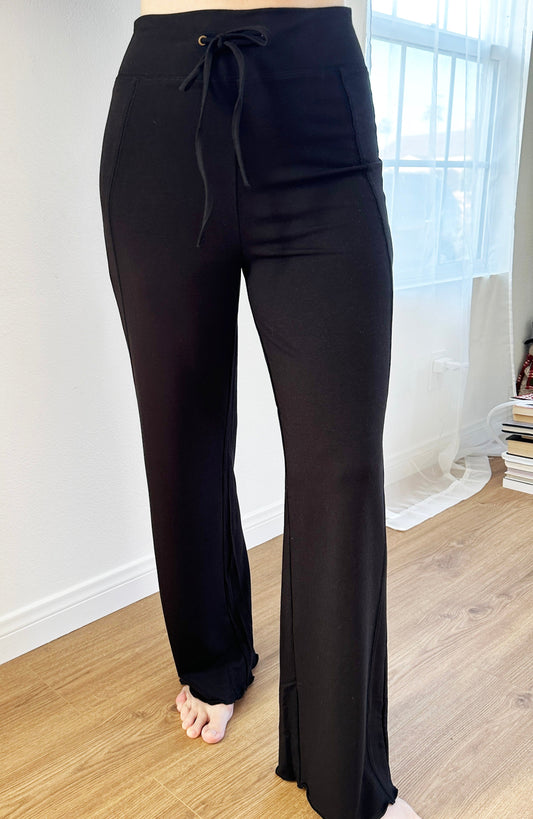 Black pants with a drawstring waist on a wooden floor.