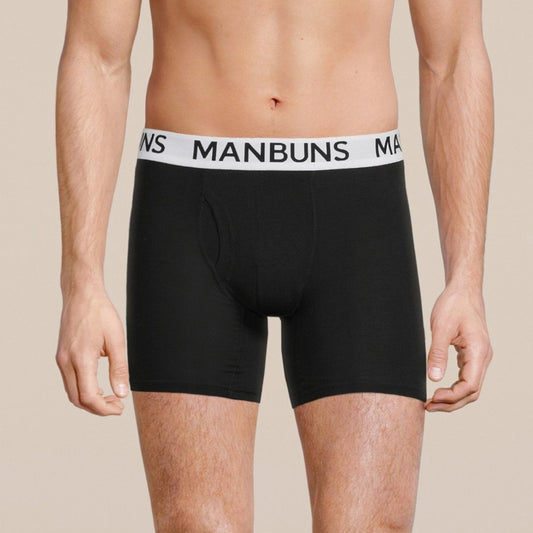 Black boxer briefs with a white 'MANBUNS' waistband on a beige background