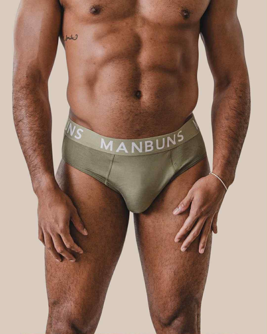 Man wearing olive green underwear with 'MANBUNS' branding on a beige background